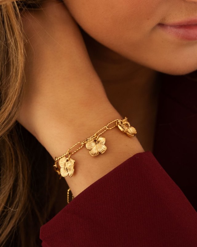 Model draagt gouden schakelarmband met bloemetjes