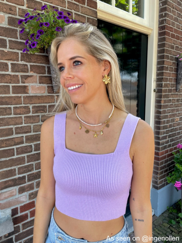 Meisje met lila top en bloem oorbellen gecombineerd met een bedelketting en een parelketting