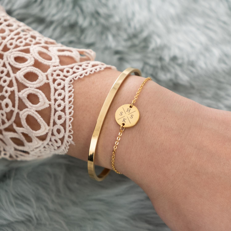 Pols met gouden armbandjes initialen en open bangle