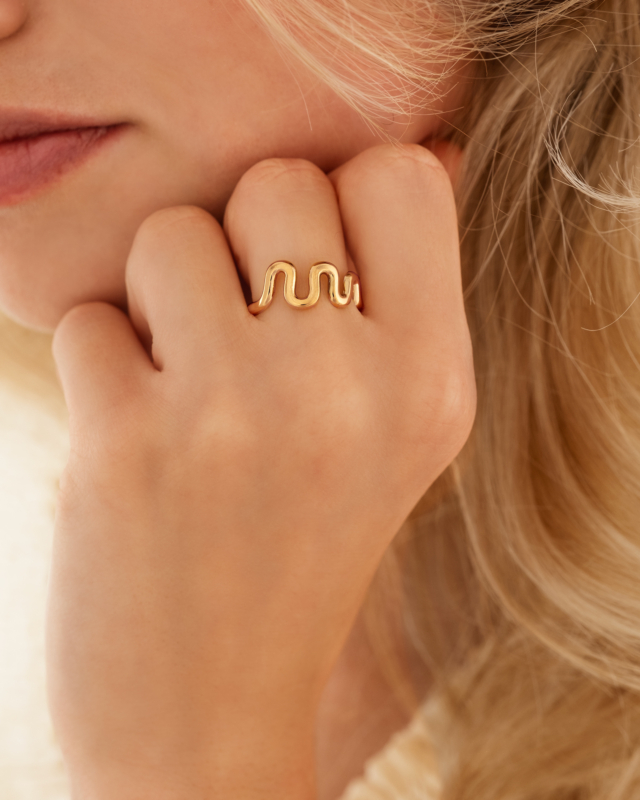 Model draagt gouden ring met golven