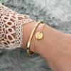 Pols met gouden armbandjes initialen en open bangle