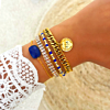 Model draagt gouden armbanden met blauwe details